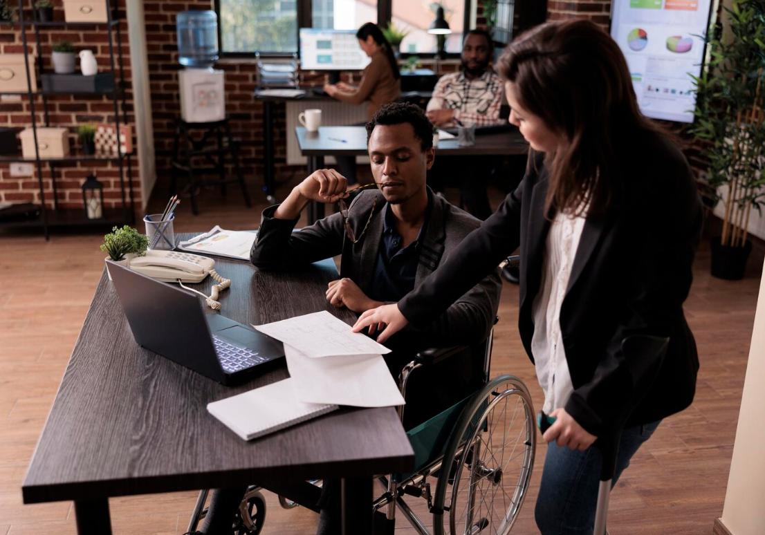 woman in crutches looking at papers on desk with man in wheelchair