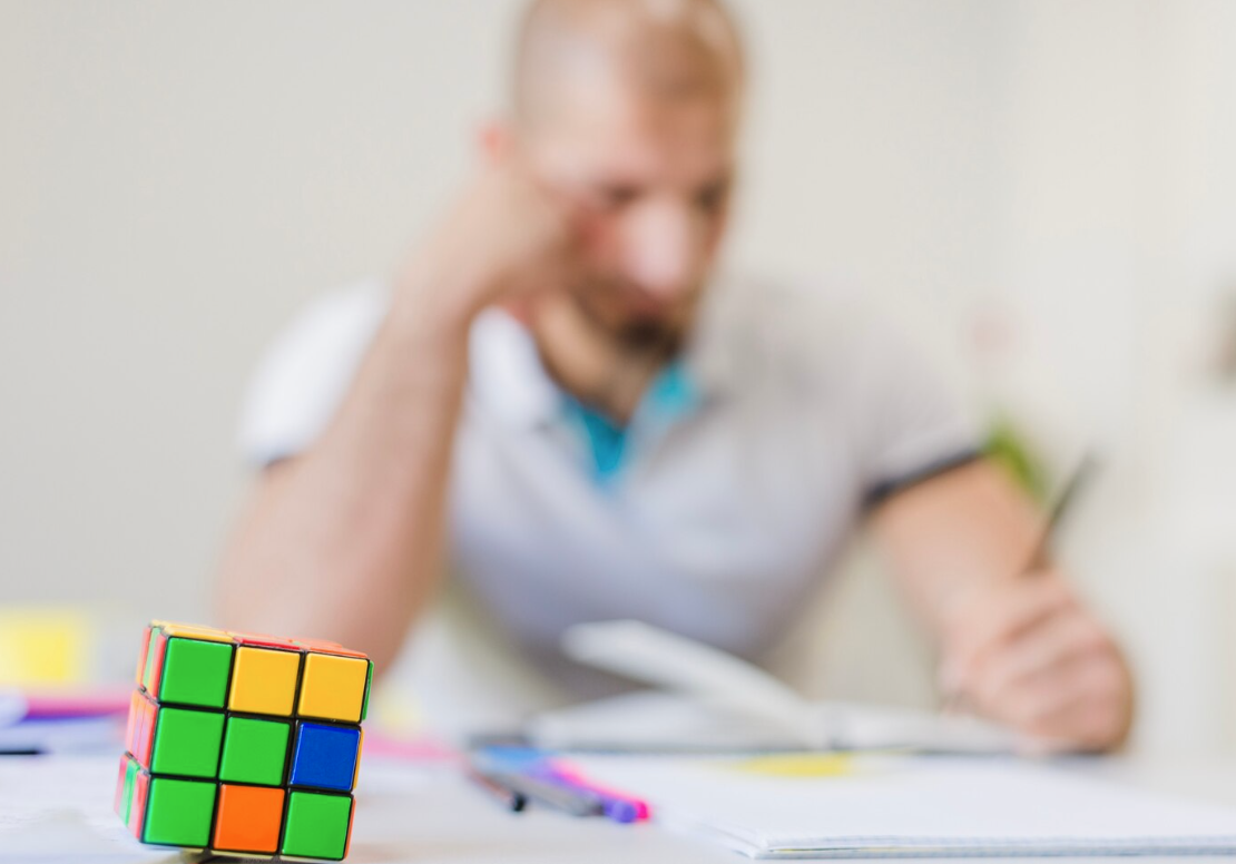 blurrred image of man working with rubics cube on desk