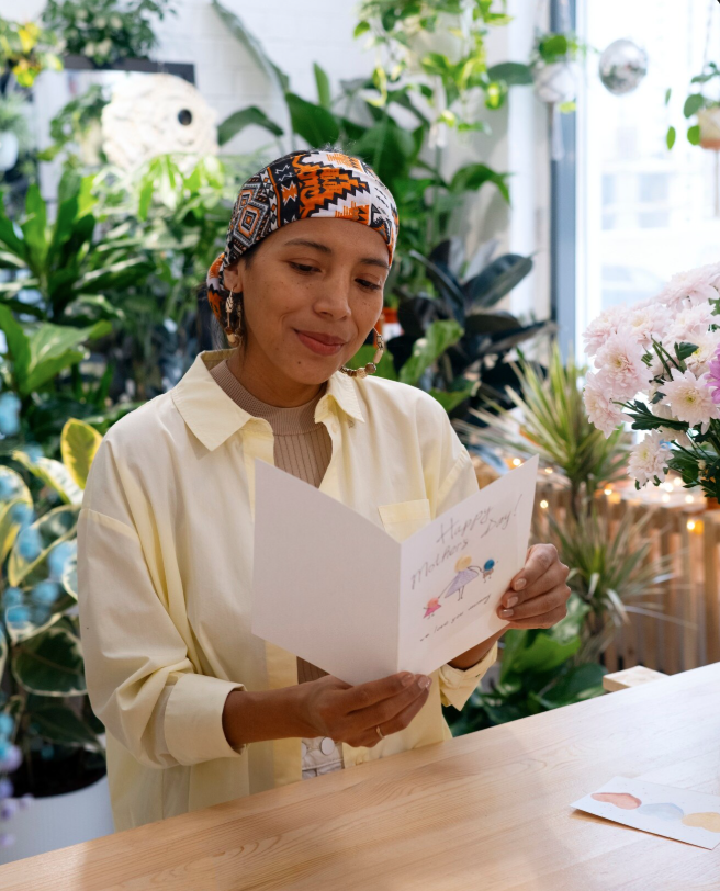 woman with tribal head clothe in office with plants reads card