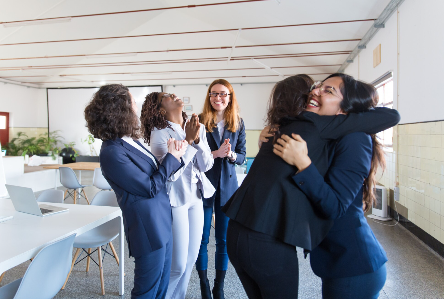 women in suits hug and celebrate together