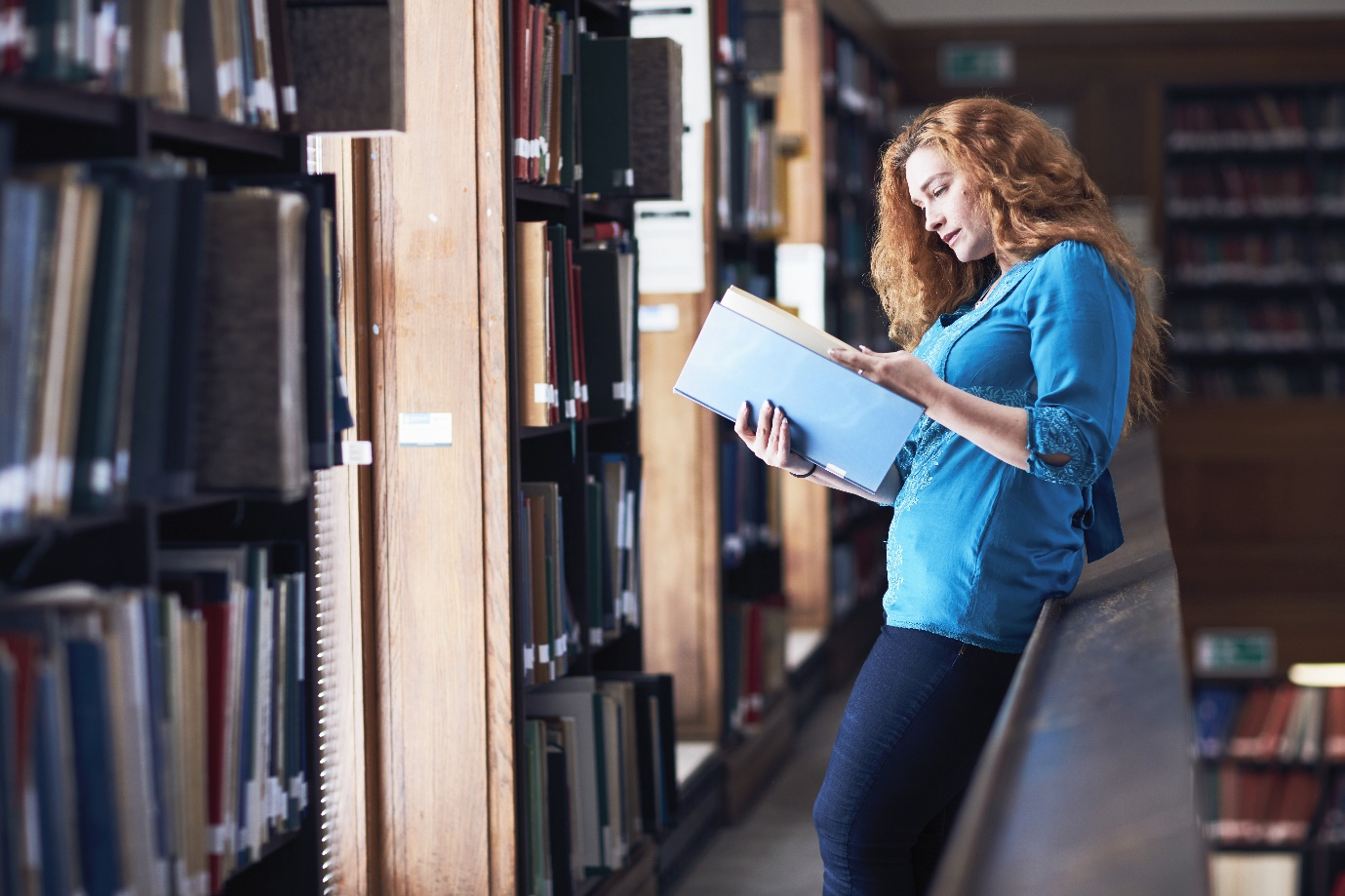 A person reading a book in a library

Description automatically generated