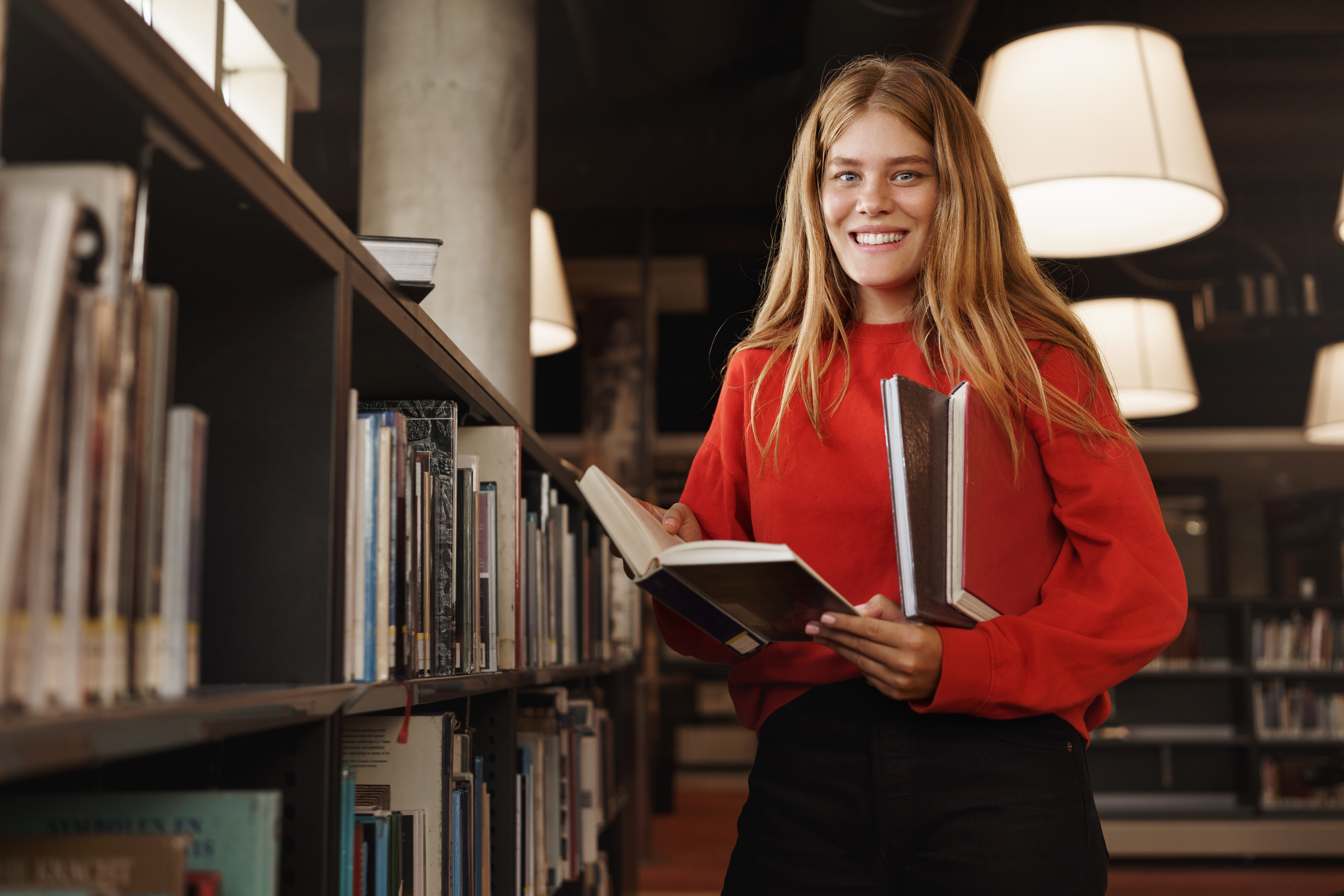 student in library smiling with books